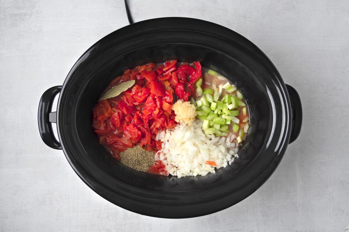 overhead shot of a black slow cooker with ingredients inside; the slow cooker is on a grey surface