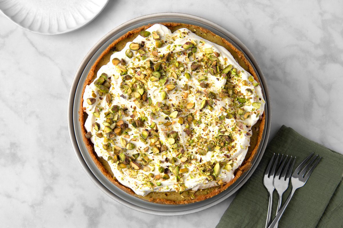 chopped pistachios sprinkled on whipped cream spread on top of cheesecake