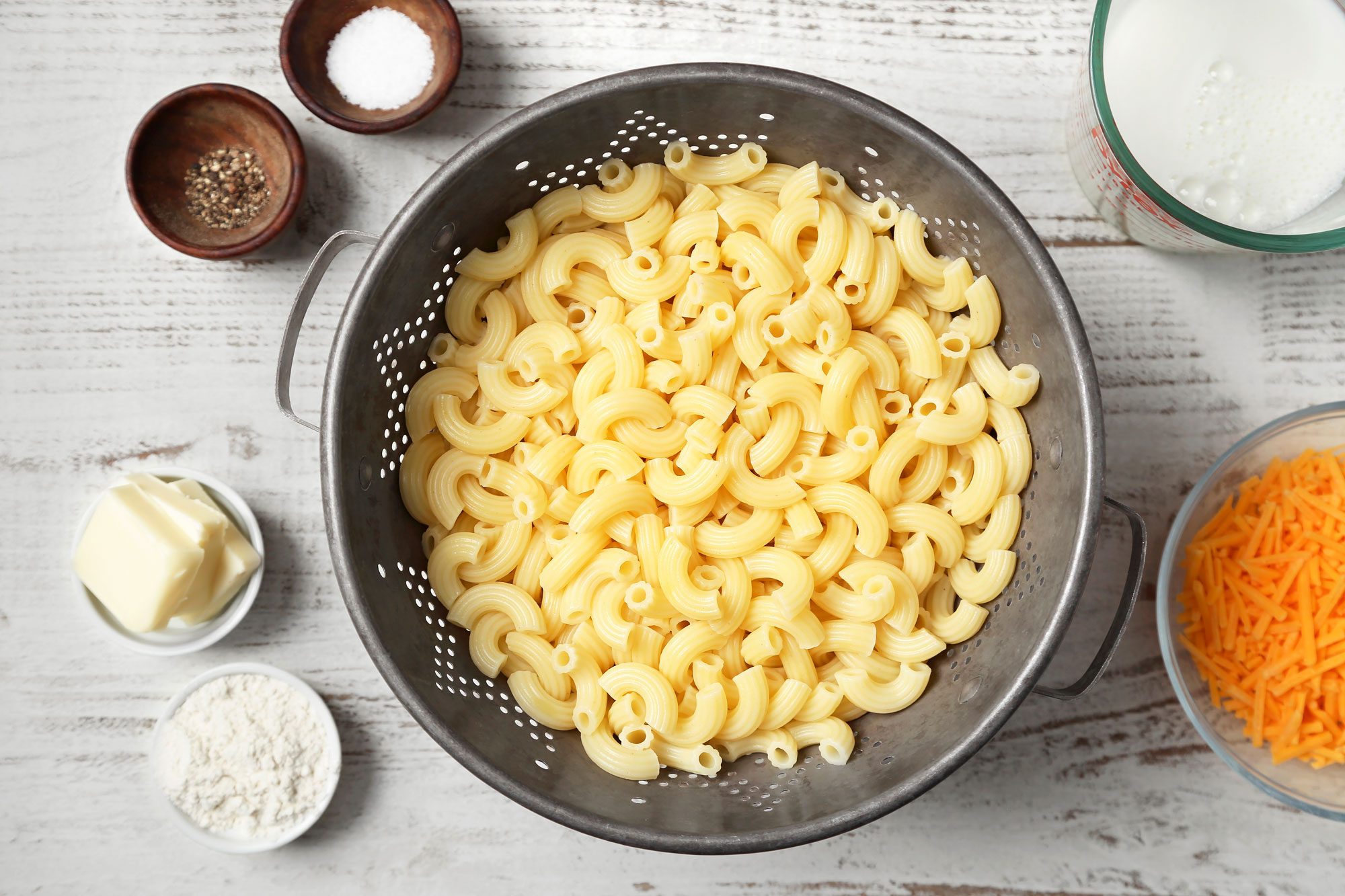 Mac and cheese ingredients placed over white wooden background