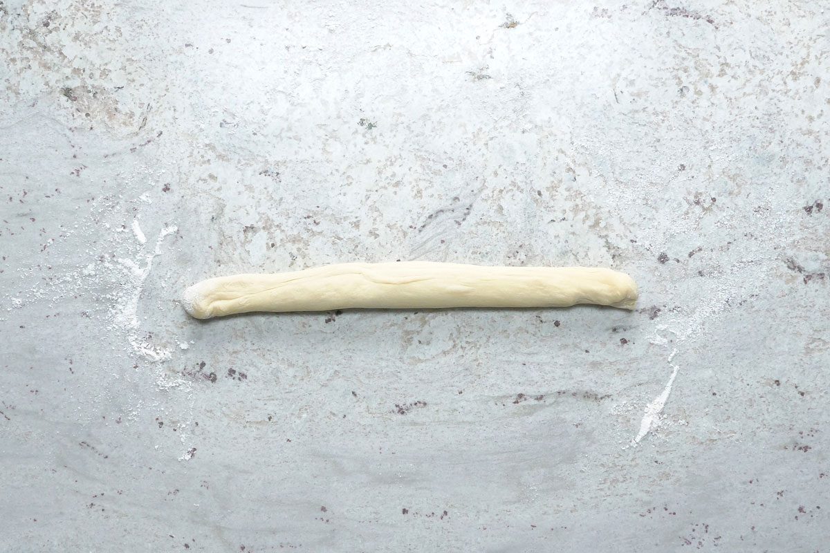 Overhead shot; punch down dough; Turn onto a lightly floured surface; divide into 6 portions; Roll each portion into a rope; grey surface;