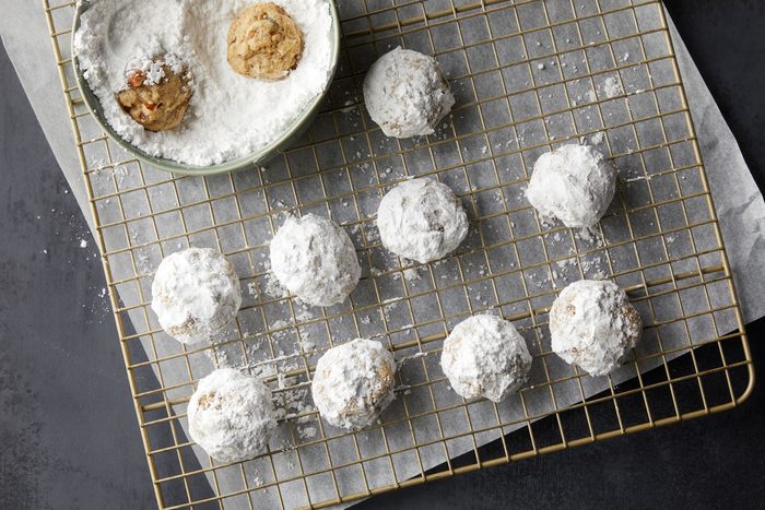 Rolling baked cookies in confectioners' sugar and placing on wire racks