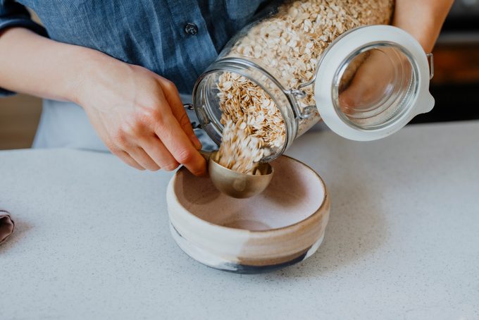 Hands of a Woman Putting Rolled Oats into a Bowl
