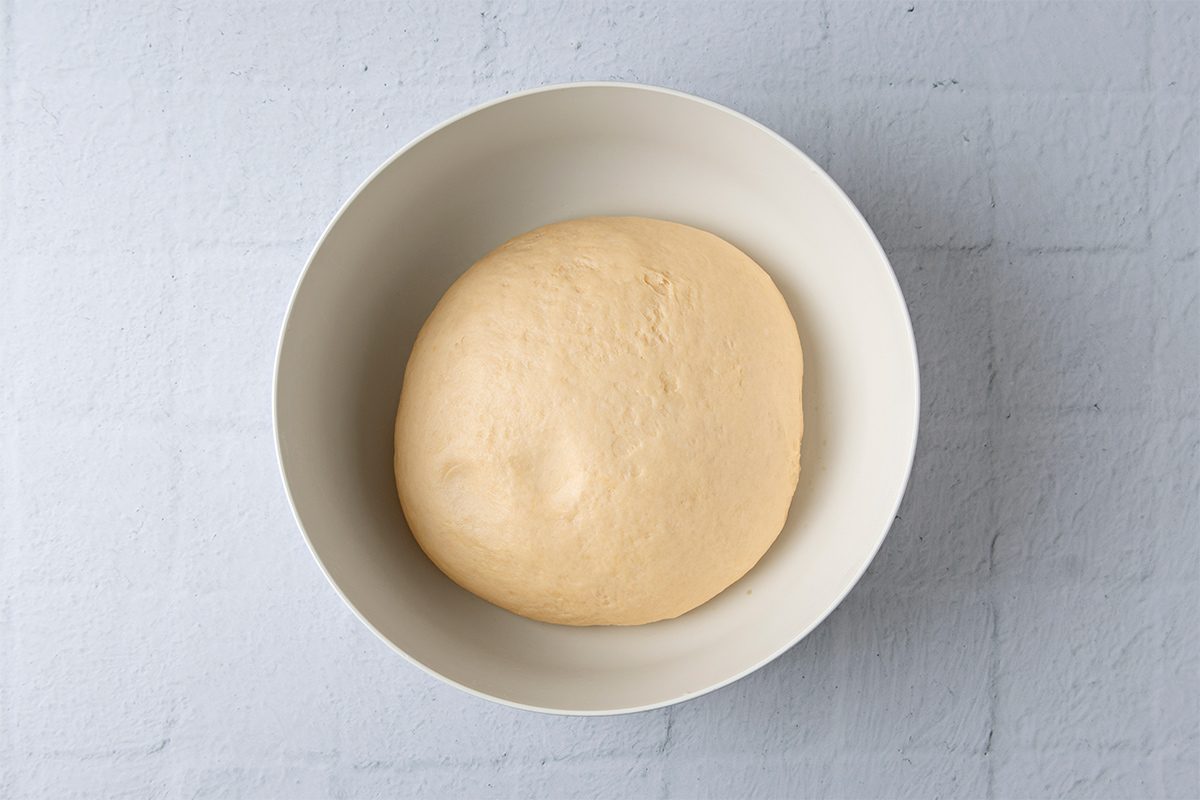 Six unbaked dough rings are evenly spaced on a floured metal baking sheet. The dough rings are light in color and are arranged in two rows of three, positioned against a light blue textured background.