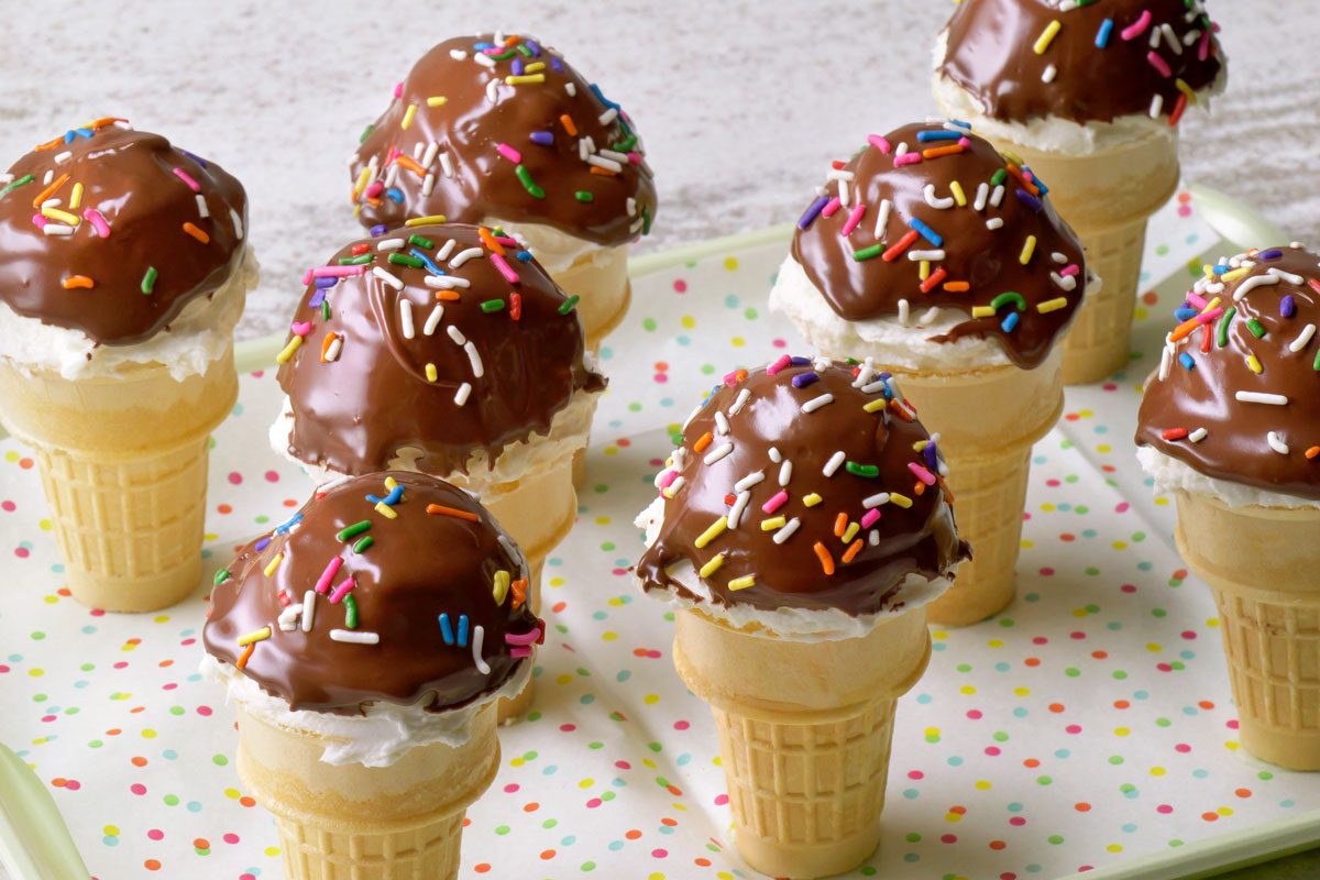 3/4th shot of a tray of ice cream cones dipped in chocolate and decorated with sprinkles; the cones are arranged on a tray with a colorful polka dot design