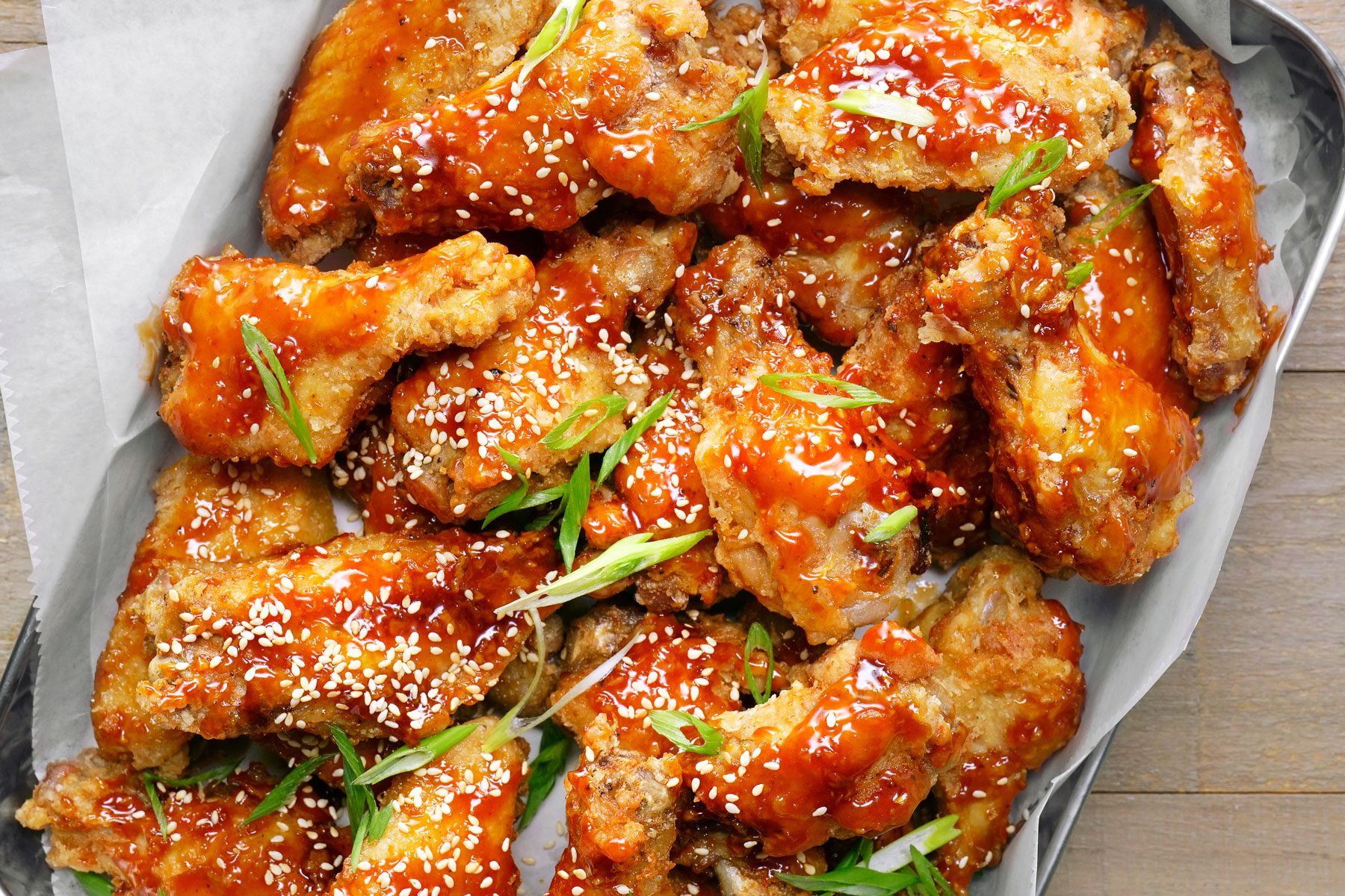 A plate of fried chicken wings coated in a sweet and spicy sauce and sprinkled with sesame seeds