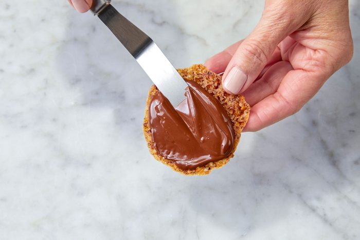 Spreading melted chocolate on baked cookie with a knife