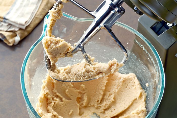 a close-up of a stand mixer with a dough hook attached to it; the hook is covered in a thick, creamy dough that looks like it's been recently mixed