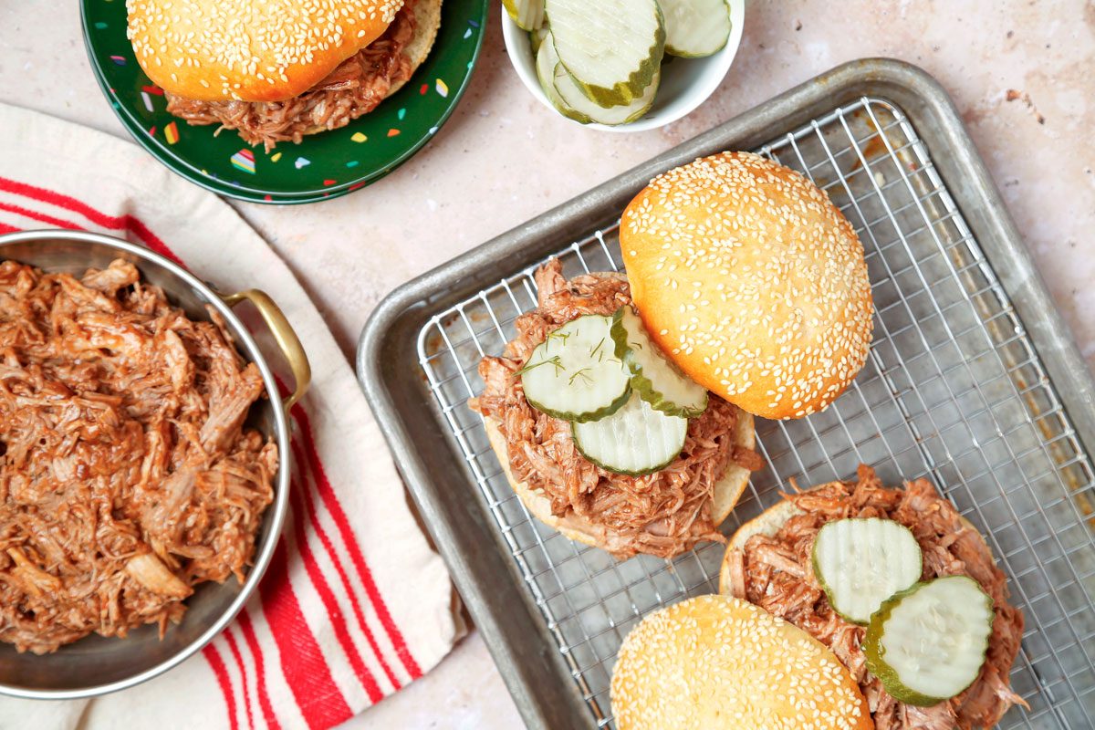 Pulled pork assembled into sandwiches on sesame seed buns with pickles; overhead