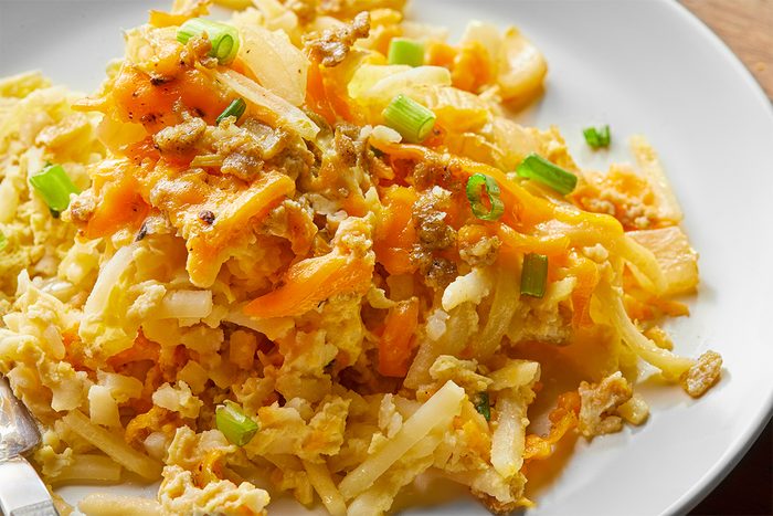 A plate of cheesy hash brown casserole garnished with green onions. The dish features shredded potatoes mixed with melted cheese and bits of onion, creating a warm, savory meal.