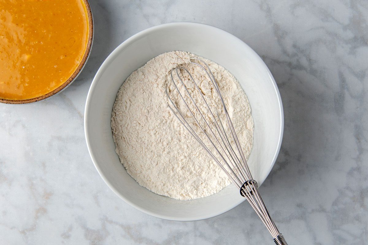 Overhead shot of a large bowl; whisk together first seven ingredients; In another bowl; combine sweet potato puree; milk; eggs; butter and vanilla extract until combined; whisk tool; marble surface;