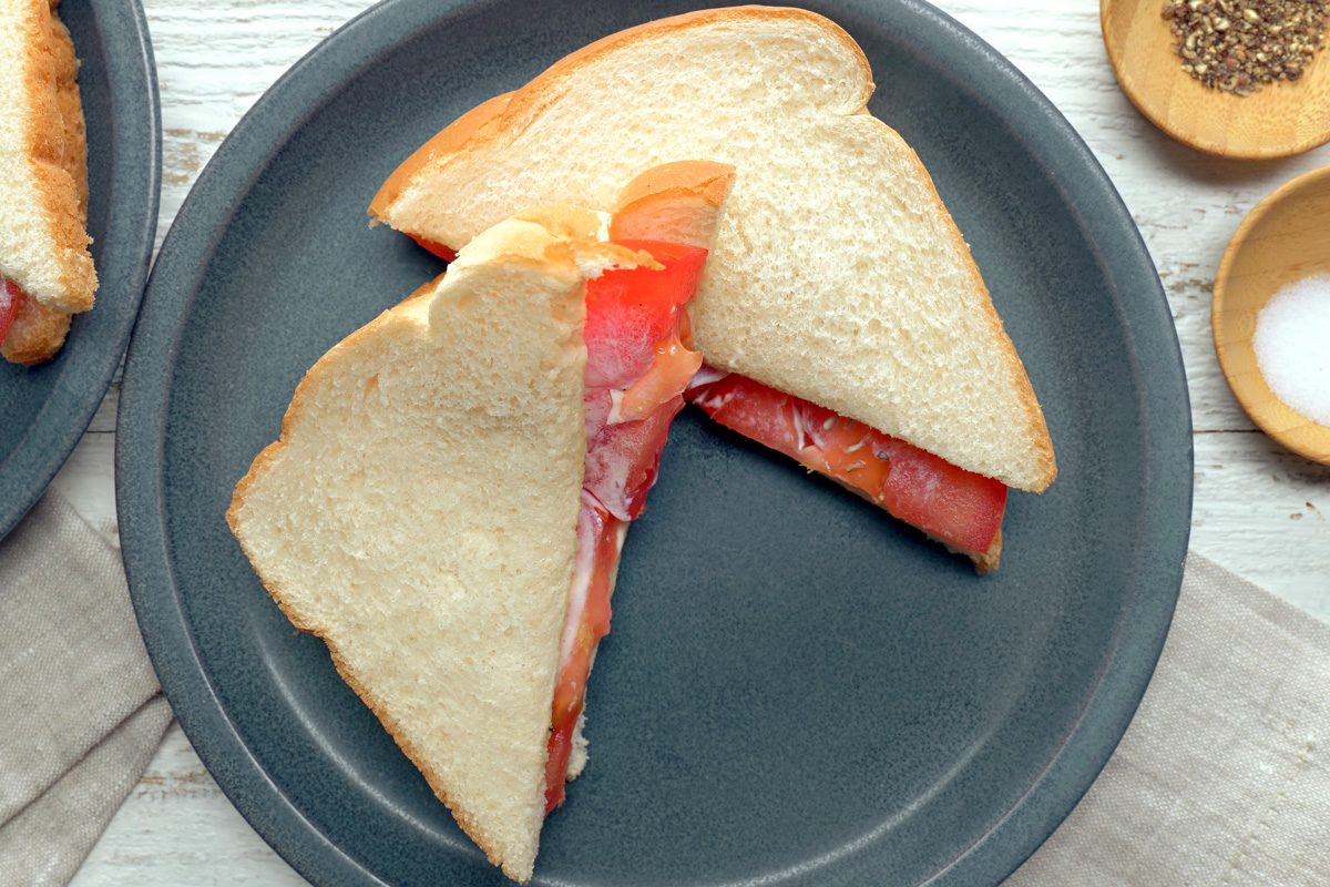 Overhead shot of Tomato Sandwich; serve on plates; napkin; small bowls of salt and pepper; white wooden surface;