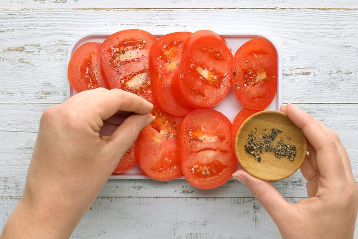 Overhead shot of season tomato slices with salt and pepper; set aside; white wooden surface;