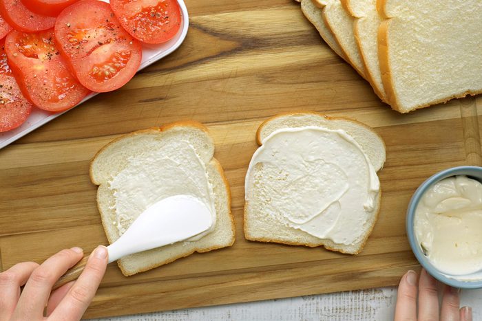 Overhead shot of spread mayonnaise on each slice of bread; wooden board; knife; white wooden surface;