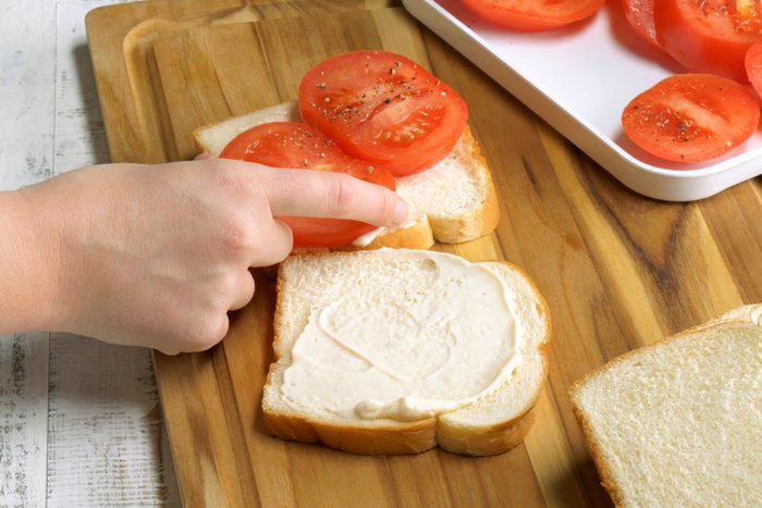 Close shot of add tomato slices to half of the slices of bread; top with the remaining slices of bread to close sandwiches; serve immediately; wooden board; white wooden surface