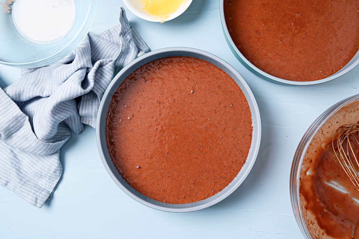 Vegan chocolate cake batter poured into greased round cake pans.