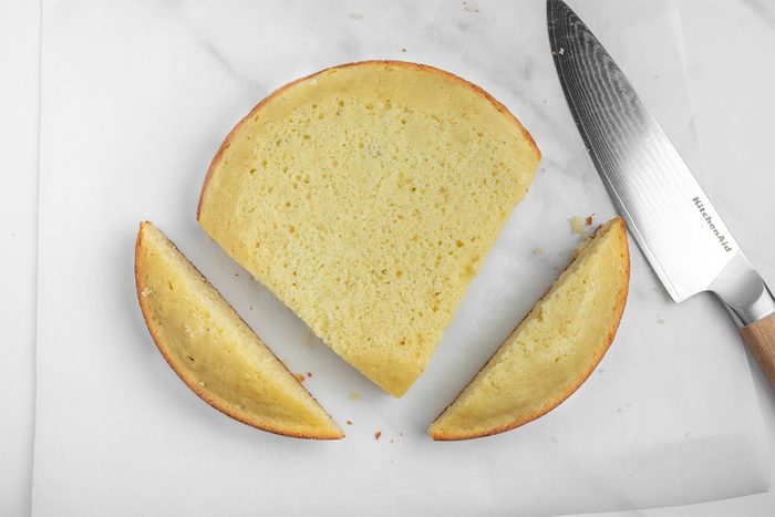 A round cake is cut into three pieces on a white surface. Two smaller, wedge-shaped pieces flank a larger semicircular piece. A silver knife with a wooden handle is placed beside them.