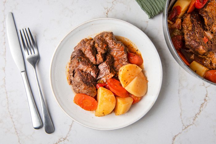 Yankee Pot Roast in a serving plate with spoon and fork on the side