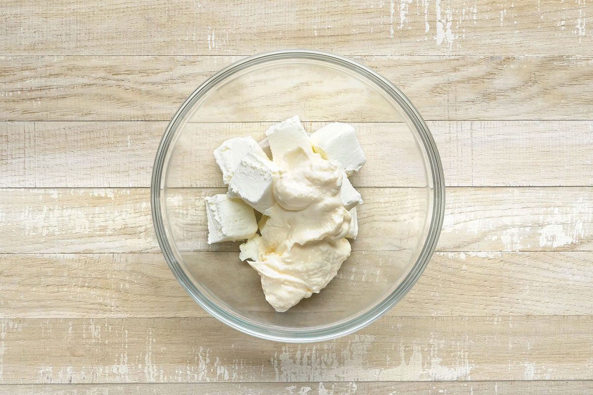 overhead shot of a glass bowl filled with cream cheese and mayonnaise, the bowl is sitting on a light brown wooden table