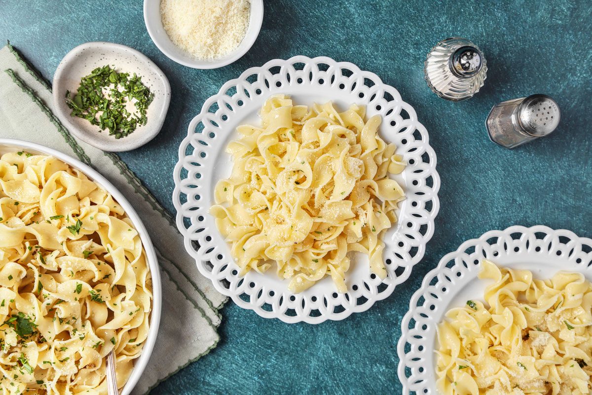Overhead shot of Buttered Noodles; In a large white bowl; served on plates; napkin; teal green surface;
