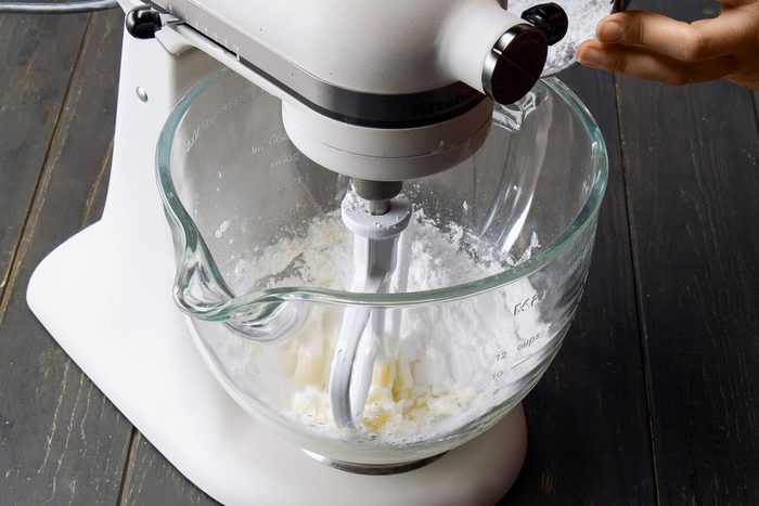 3/4th shot of a stand mixer set against a dark wooden surface; the glass mixing bowl clearly shows the ingredients being blended together