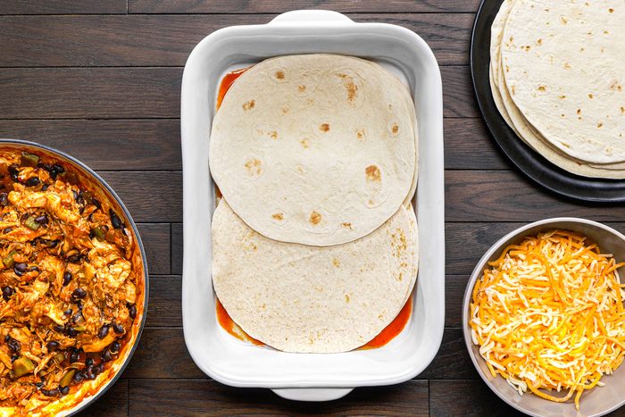 overhead shot of a white rectangular baking dish in the center contains two tortillas layered with red sauce