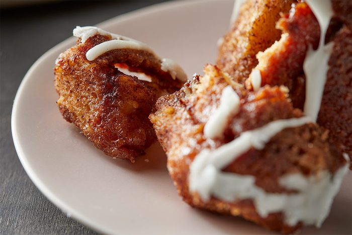 a close-up shot of a portion of a monkey bread, on a light colored plate; the focus is on two pieces of the dessert, one slightly separated from the rest, revealing the soft, textured interior; a white, creamy icing is drizzled over the top, the background is blurred