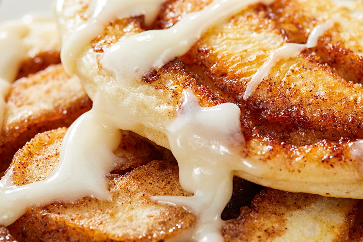 Close-up of a cinnamon roll topped with creamy icing. The roll features visible swirls of cinnamon and a golden-brown crust, with the icing drizzling over the edges, creating a rich, indulgent appearance.