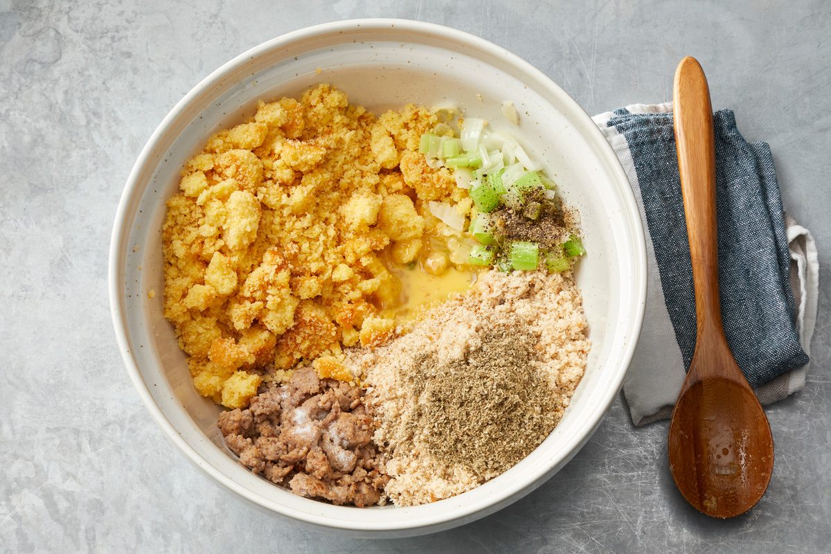 Overhead shot of combine cooked vegetables with bread crumbs; eggs; seasonings; cornbread and sausage; wooden spoon; napkin; marble surface