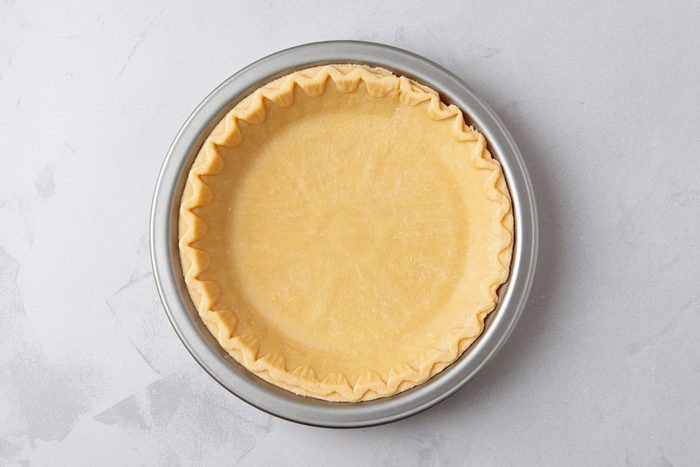 overhead shot of of a pie crust in a metal pie pan on a light gray countertop