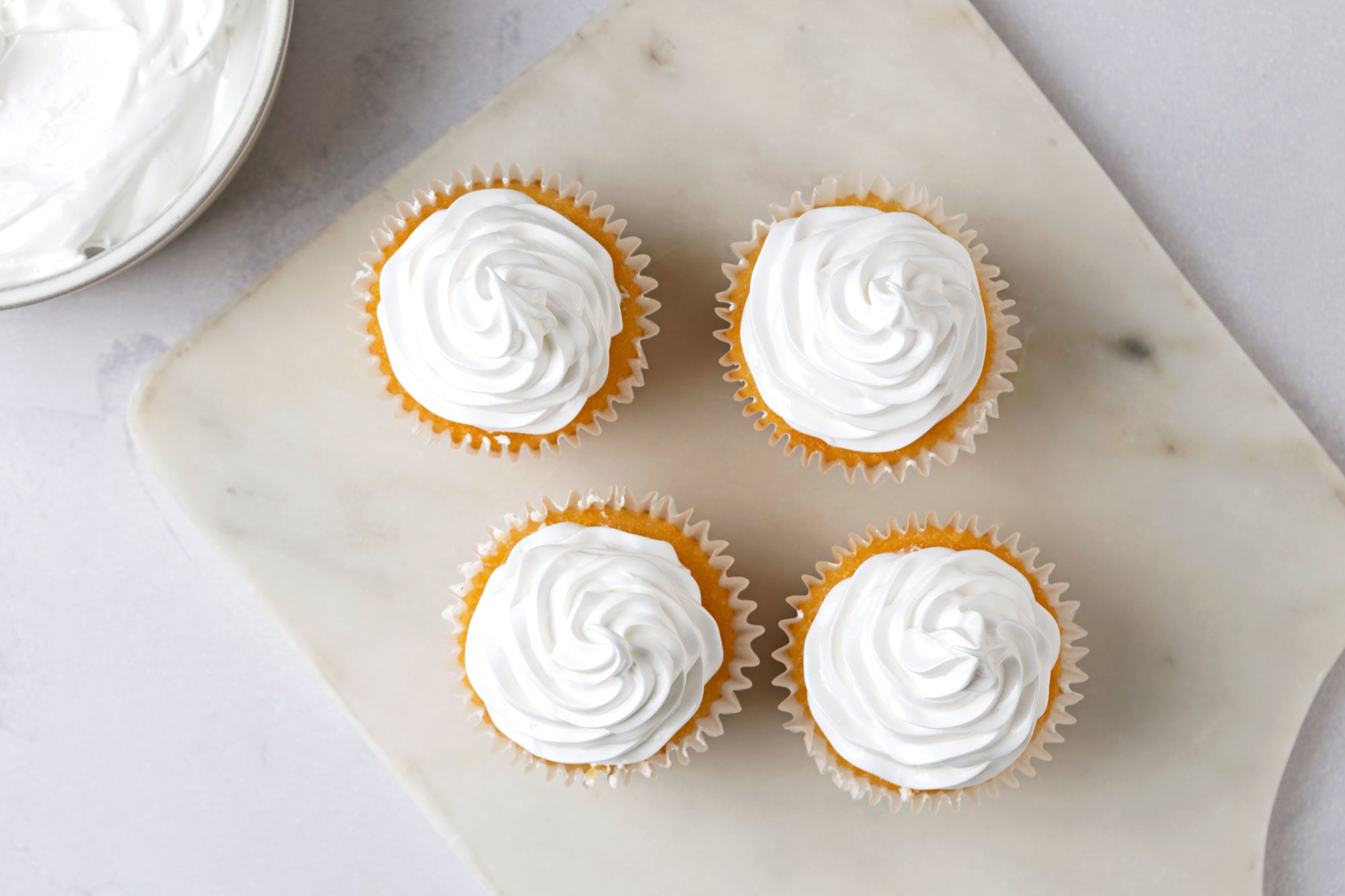 Overhead shot of Fluffy White Frosting; in a large bowl; served on cup cakes; marble surface;