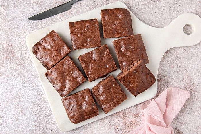 Overhead shot of Easy Gluten Free Brownies; place on white tray; knife; napkin; light brown marble surface
