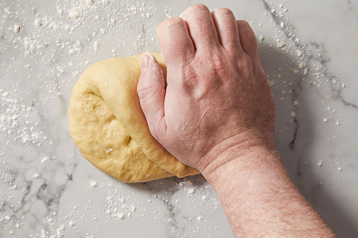 a close-up of a hand kneading a ball of dough on a marble countertop