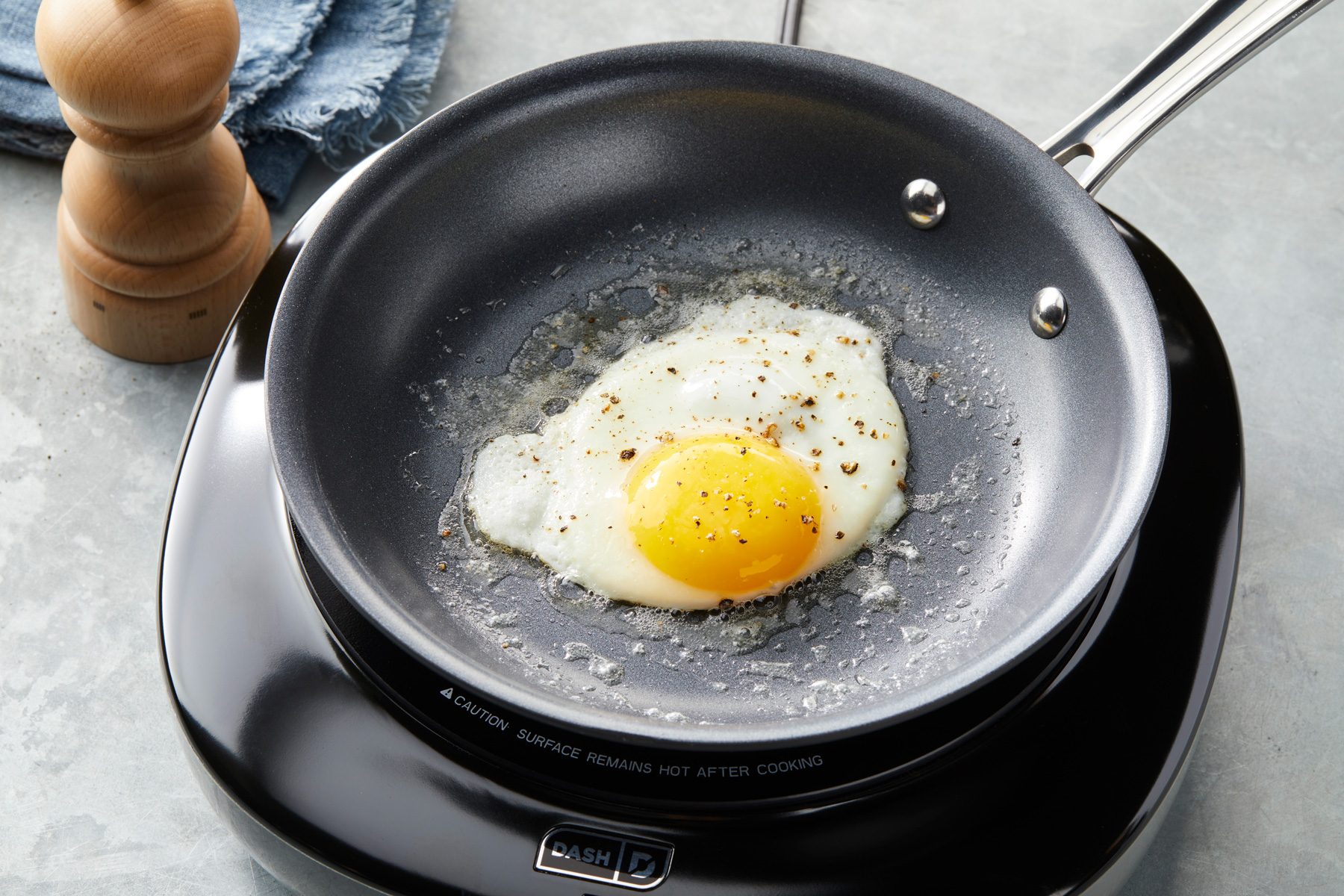 3/4 angle view shot of crack eggs into the skillet; season with salt and pepper; cook 2-3 minutes or until whites are set; induction; napkin; grey surface;