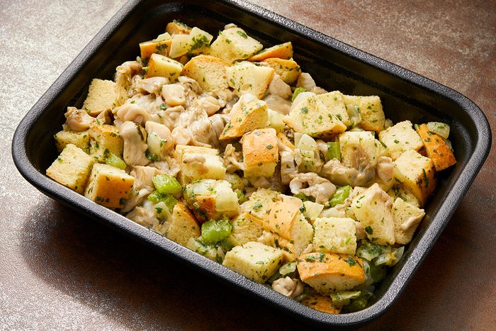 A baking tray filled with homemade stuffing. The dish contains chunks of bread, pieces of chicken, and sliced celery, all seasoned with herbs.