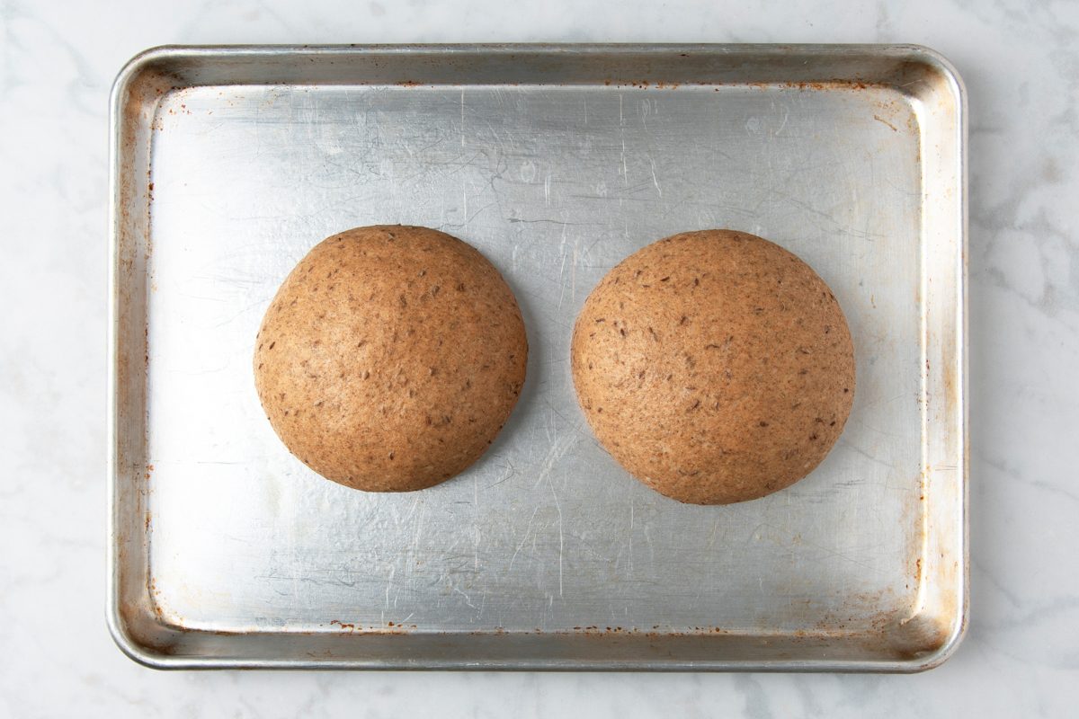two pieces of dough shaped into rounded loaves placed on a baking sheet
