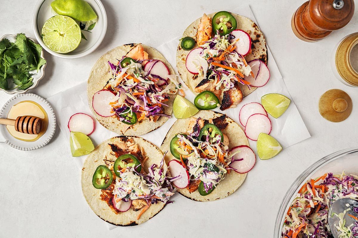 Tacos filled with cooked salmon, radishes, jalapenos, and coleslaw placed on a parchment paper.