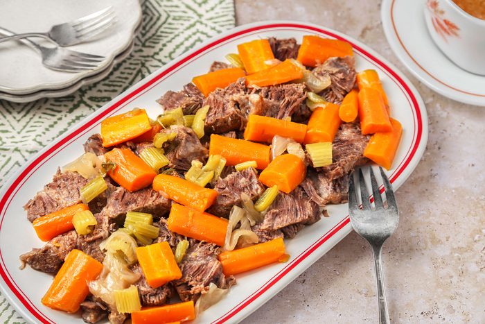 Sauerbraten sliced and served on a platter with vegetables and sauce on the side