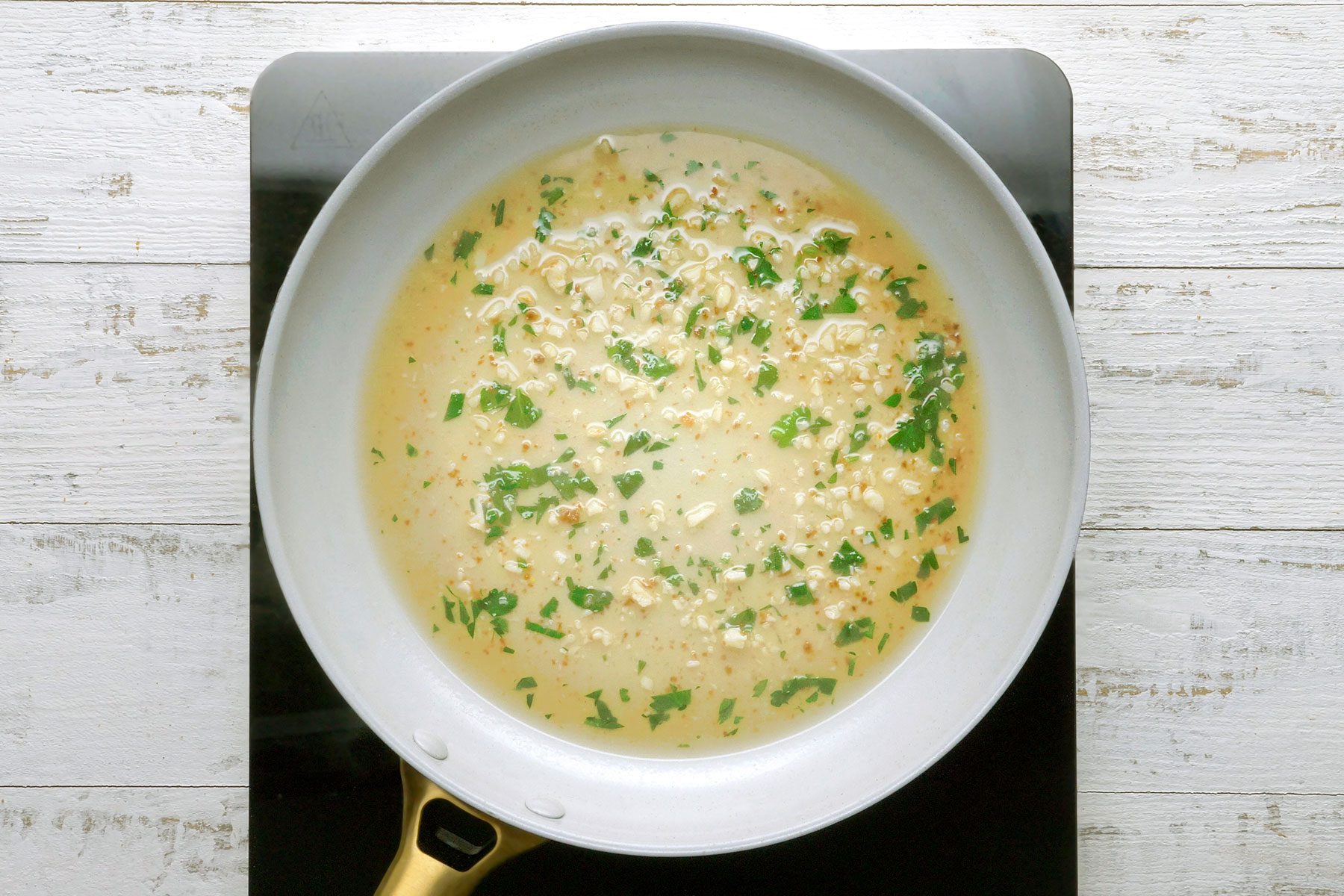 A white frying pan filled with a creamy sauce with chopped herbs and small pieces of mushroom.