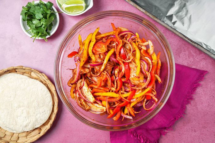 Chicken and peppers in a large bowl tossed with oil and seasonings