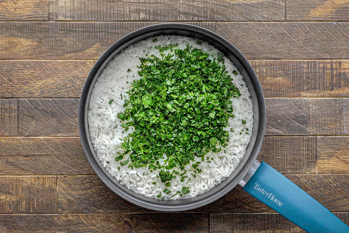 overhead shot of a black, oval-shaped frying pan on a wooden surface, filled with white rice and chopped parsley; the rice is covered in a generous amount of chopped parsley