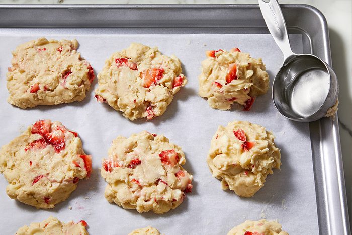 Overhead view of flattened cookie dough onto a parchment paper-lined baking sheet using the bottom of a measuring cup.