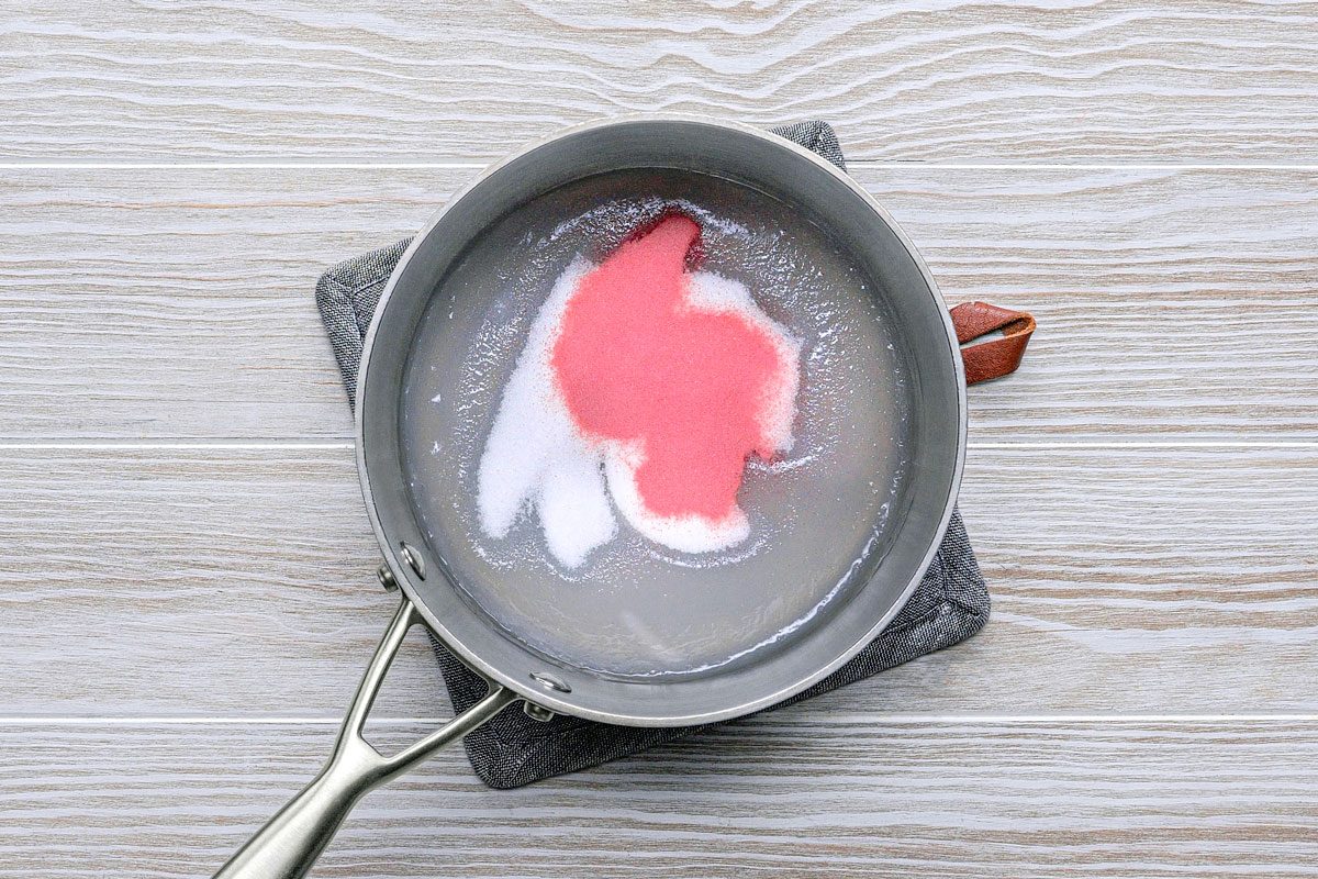 overhead shot of a metal pan with a long handle, the pan is placed on a grey and black potholder; inside the pan there is a pink and white mixture; the pan is on a light wood surface