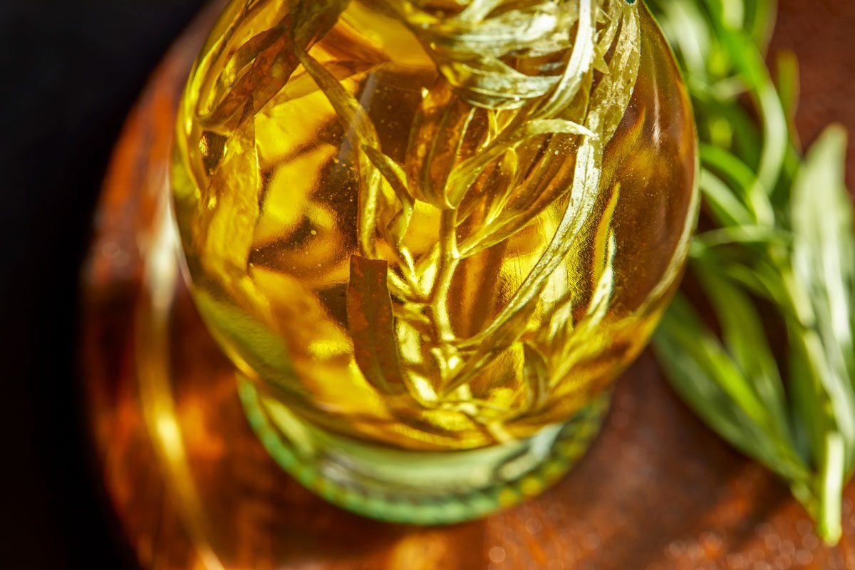 Close up view shot of Tarragon Vinegar; poured into a sterilized decorative bottle with additional tarragon; placed on a wooden tray; dark surface;