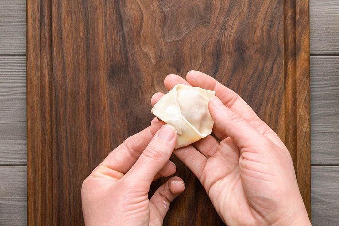 Wonton wrapper being folded in boat shape