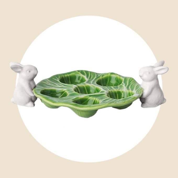 Two white bunnies holding a cabbage egg tray on a white and tan background