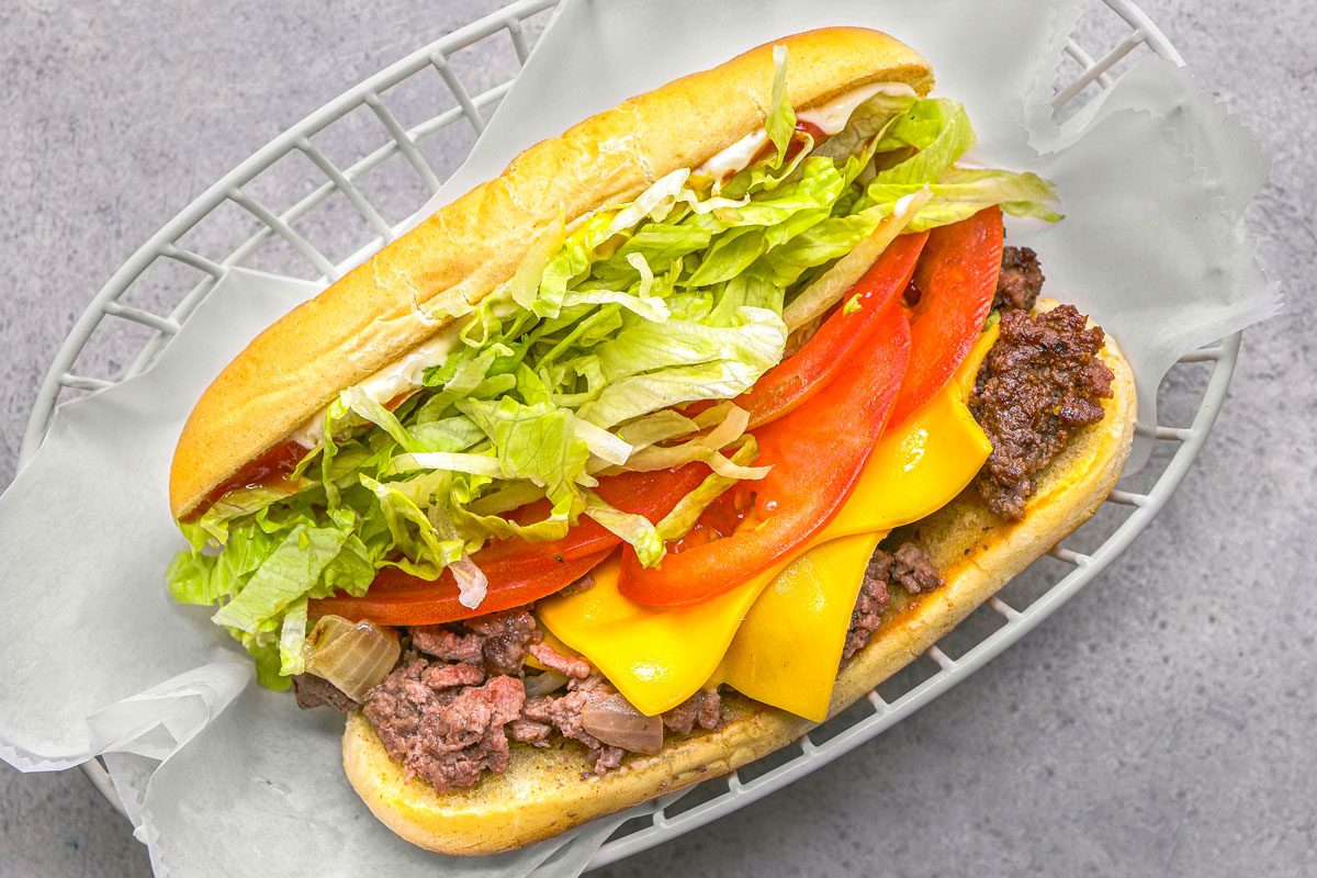 overhead shot of a fully assembled Chopped Cheese sandwich in a white wire basket lined with parchment paper, placed over a neutral grey background