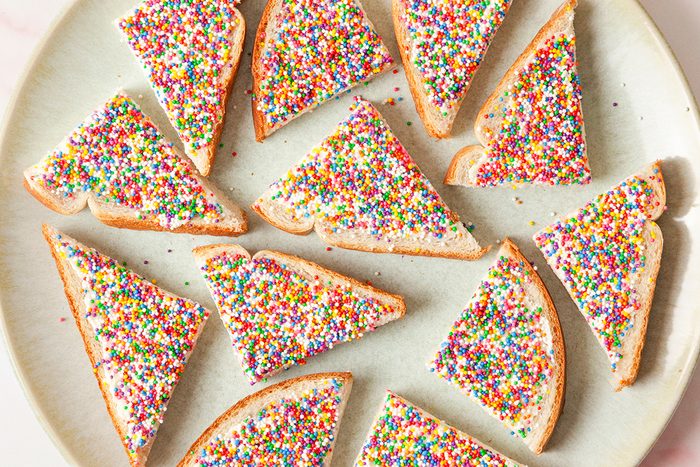 Triangular slices of bread topped with a spread and colorful sprinkles are arranged on a round white plate.