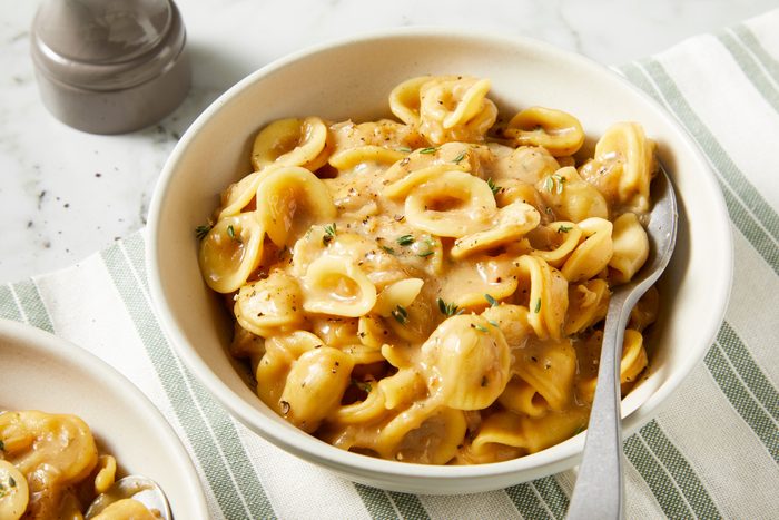 Pasta spooned into shallow bowls, garnished with shredded cheese and fresh thyme leaves, served hot.