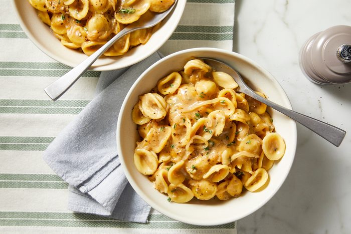 Pasta spooned into shallow bowls, garnished with shredded cheese and fresh thyme leaves, served hot.