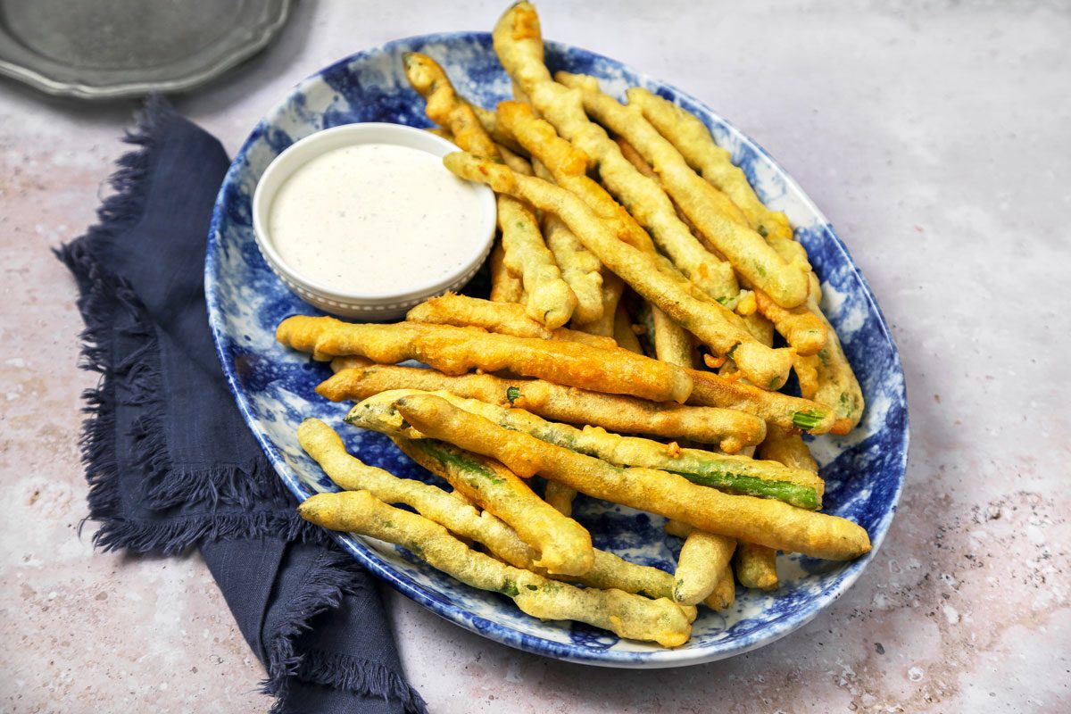 Cover push pull image of Taste of Home's Fried Asparagus recipe shot on a grey concrete surface; Battered and fried asparagus served on a platter with ranch dressing